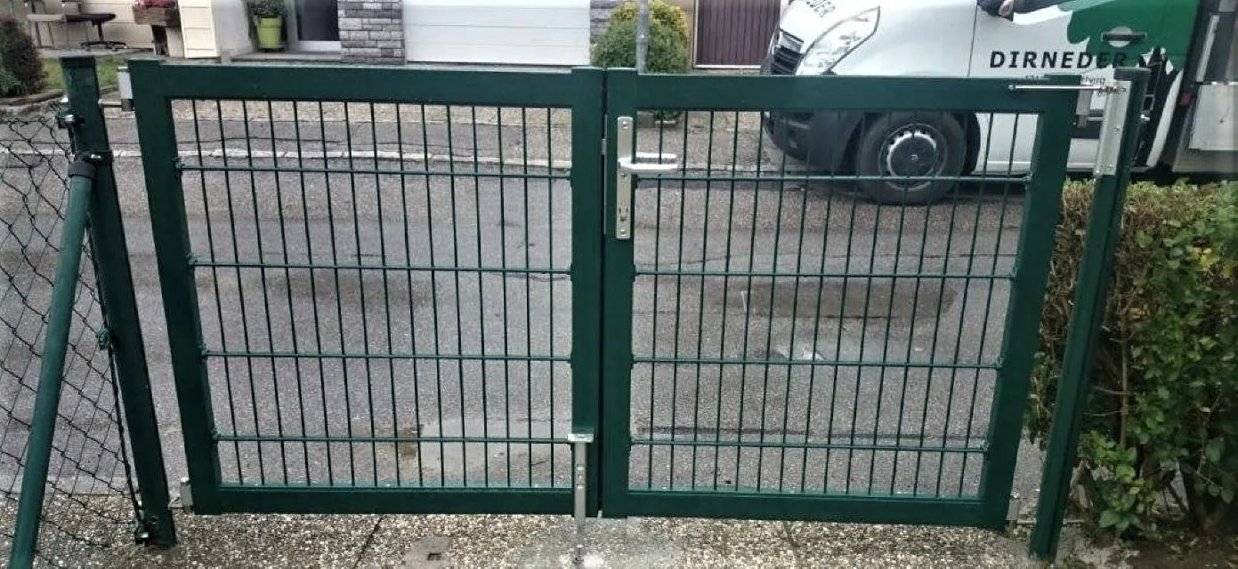 Grünes zweiflügeliges Gartentor in einem Maschendrahtzaun