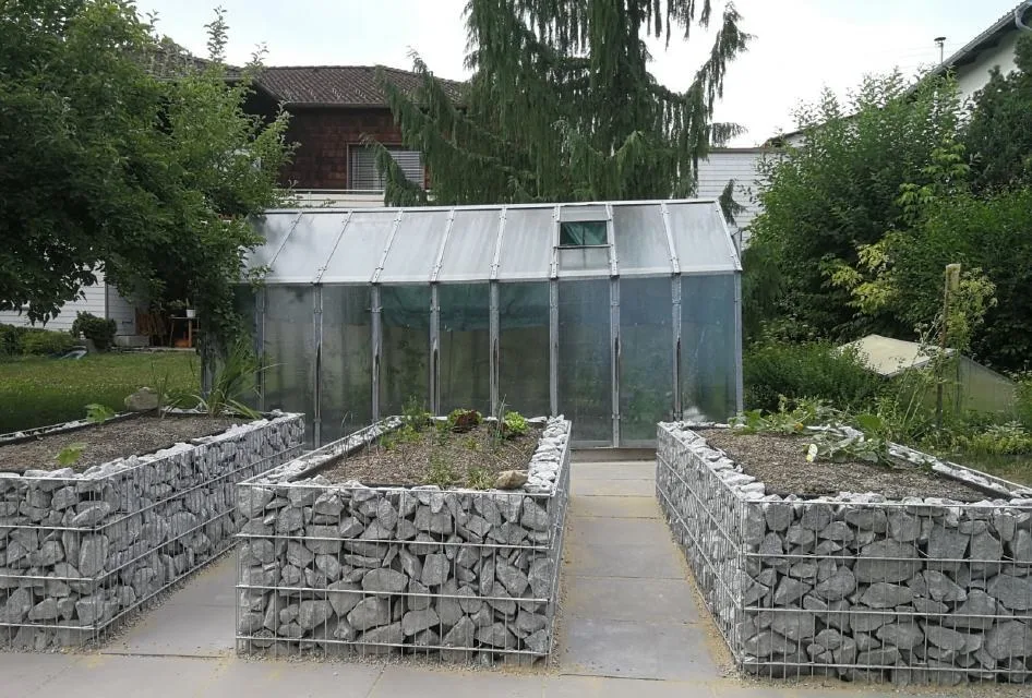 Drei Hochbeete aus Gabionen vor einem Glashaus