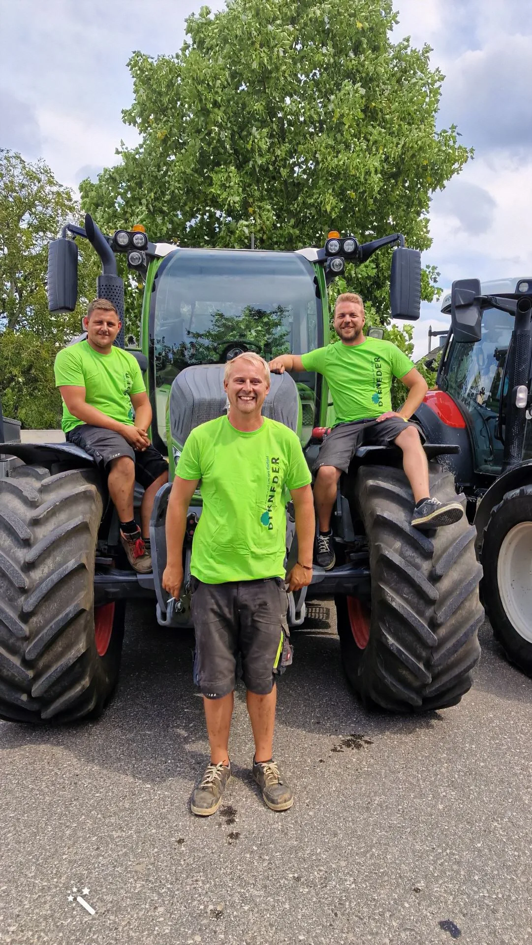 Drei junge Mitarbeiter in grünen Dirneder-Shirts auf und vor einem Traktor