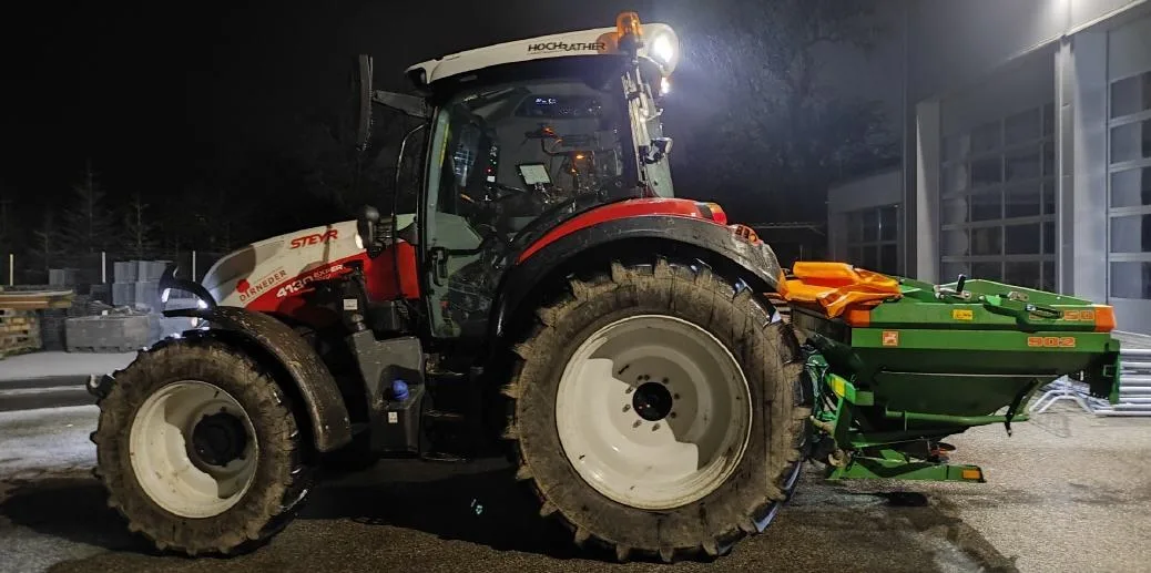 Traktor mit angebautem Salzstreuer bei Nacht