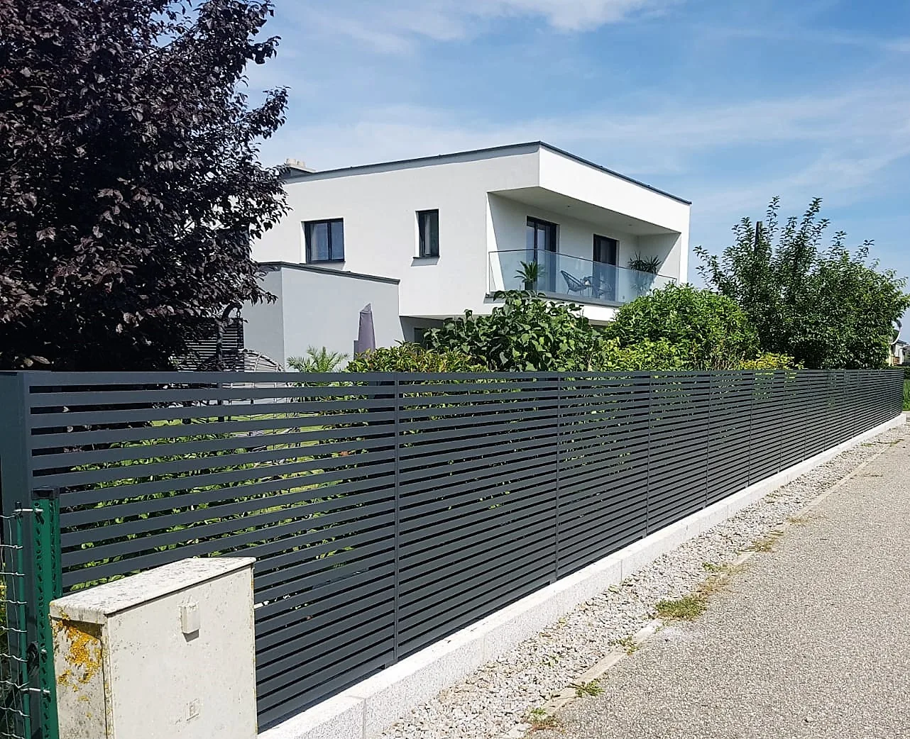 Anthrazitfarbener Lamellenzaun entlang eines Gehwegs vor einem modernen Haus